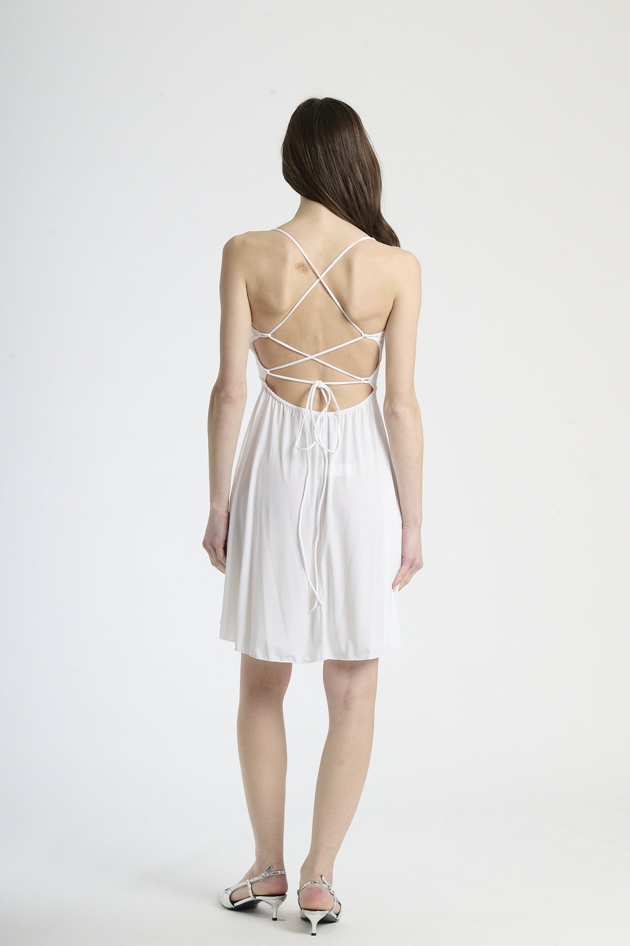 Vestito bianco in tessuto luminoso, silhouette a campana con bretelle sottili, ideale per eventi estivi e cerimonie leggere.