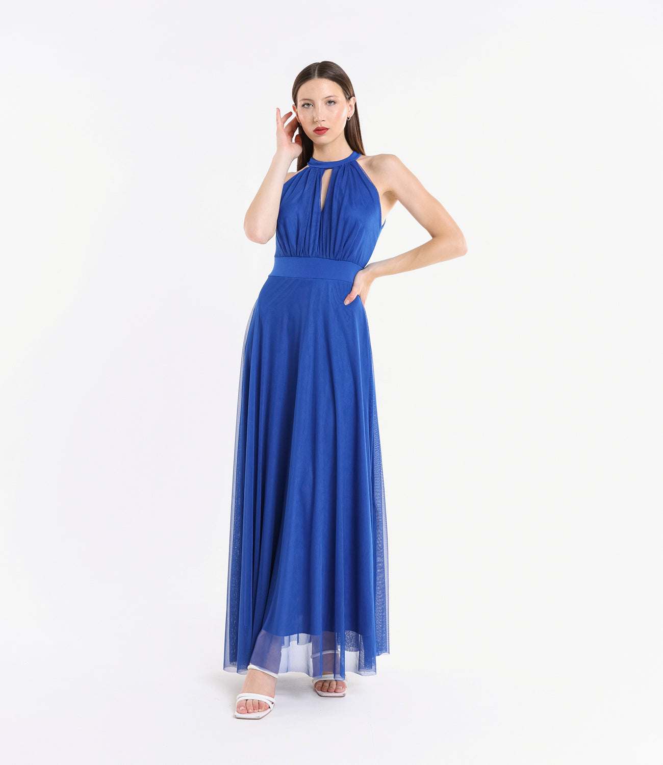 Donna con abito lungo bluette, colletto a nodo, pianta verde tropicale accanto