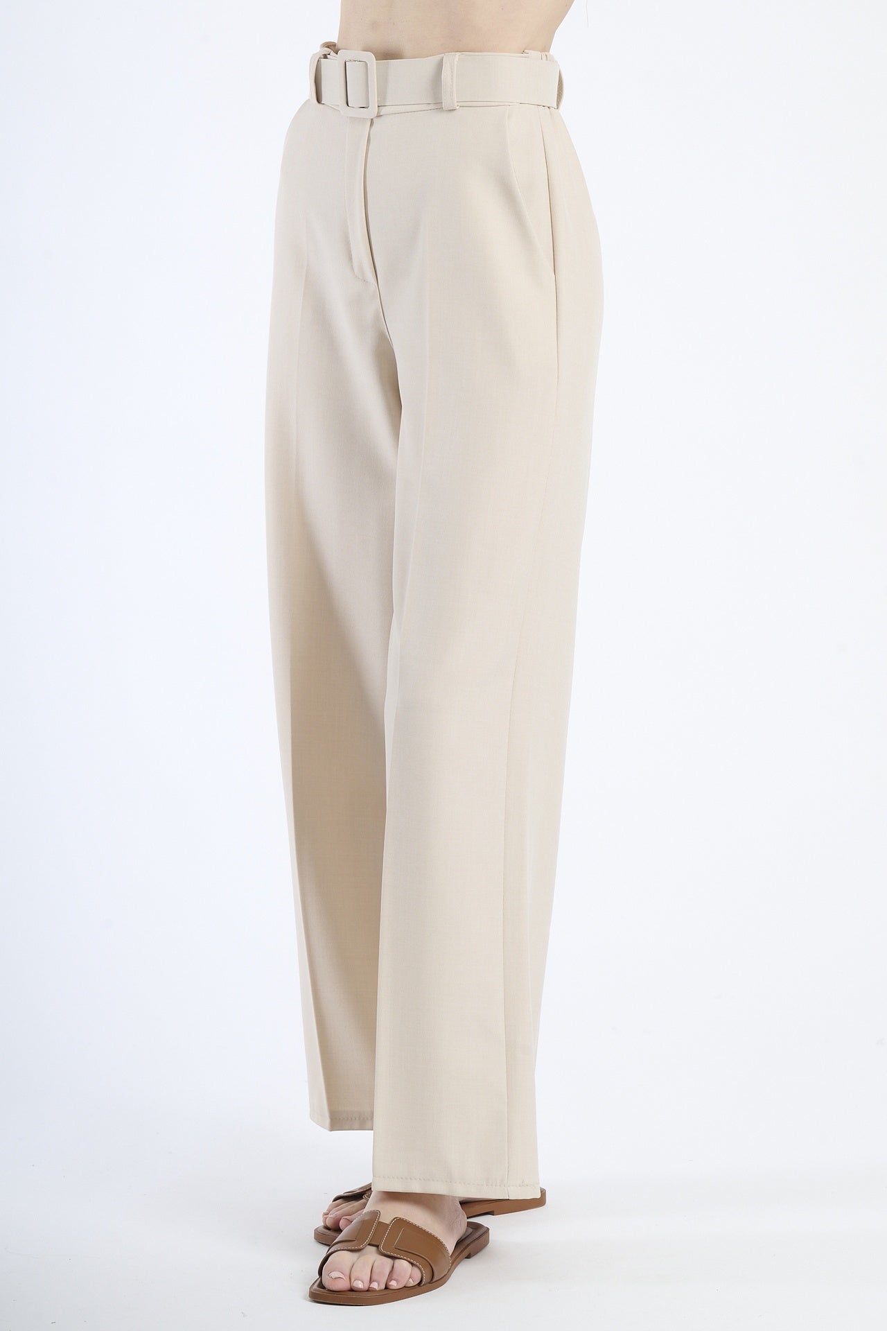 Pantaloni larghi beigi con cintura, taglio a zampa, abbinati a sandali.