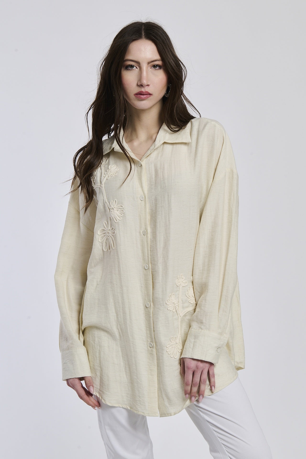 Camicia beige indossata dalla donna, con un disegno semplice e linee pulite, che sottolinea la sua personalità profonda e riflessiva.