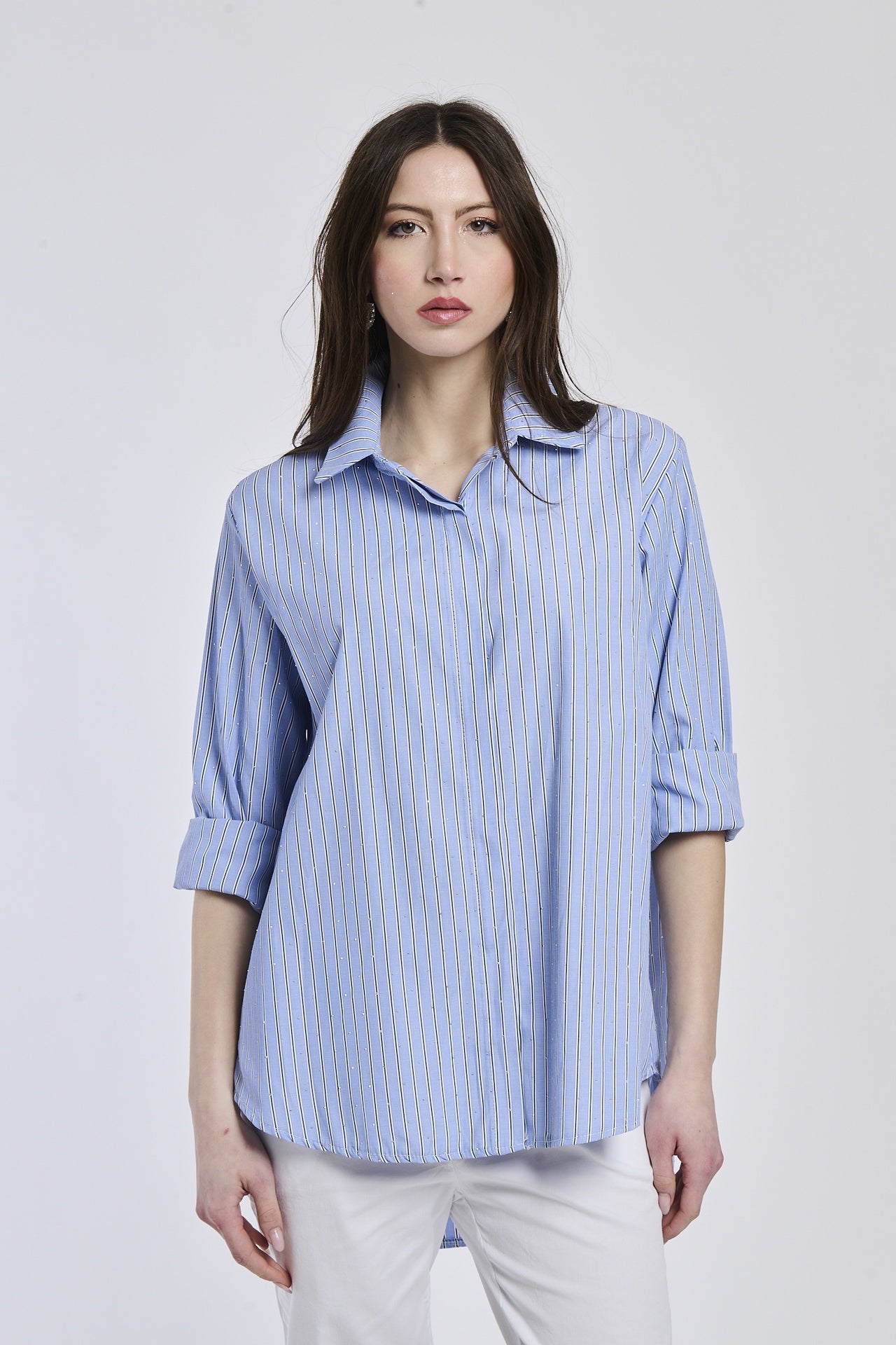 Donna con camicia a righe blu e bianche, colletto a camicia, maniche arrotolate a 3/4, taglio oversize.