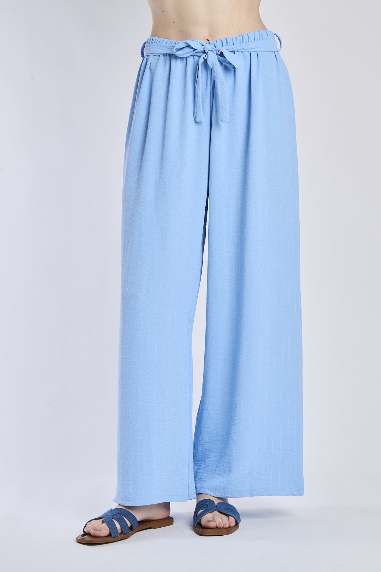 Pantaloni larghi azzurri con coulisse e nodo in vita, abbinati a sandali.