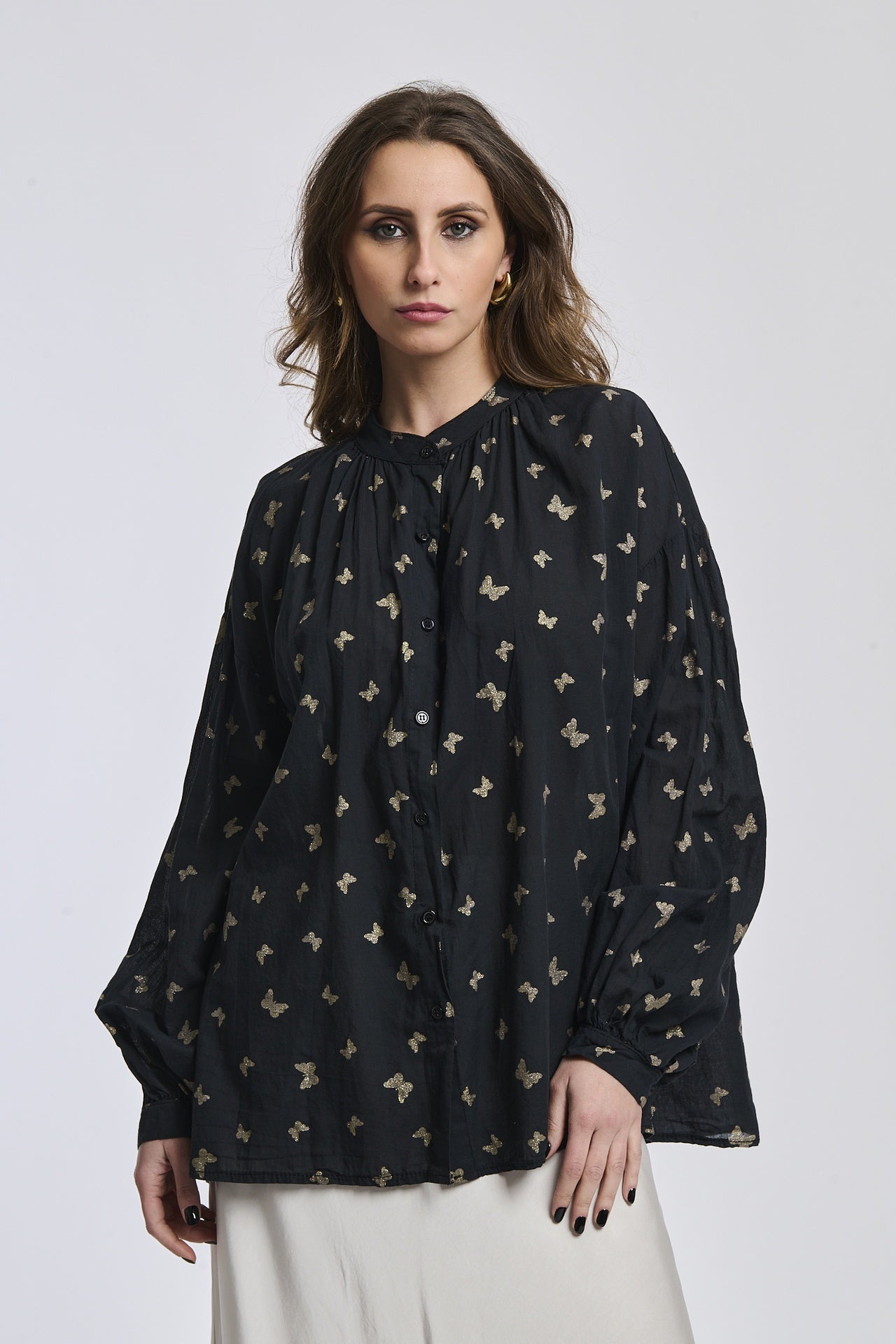 Donna con una camicia nera stampata, maniche a lanterna, collo alto e bottoni centrali, stile misterioso e affascinante.