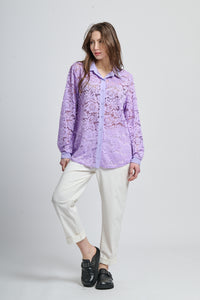 Camicetta lilla con motivi, collo camiciera e maniche lunghe, abbinata a pantaloni neri.