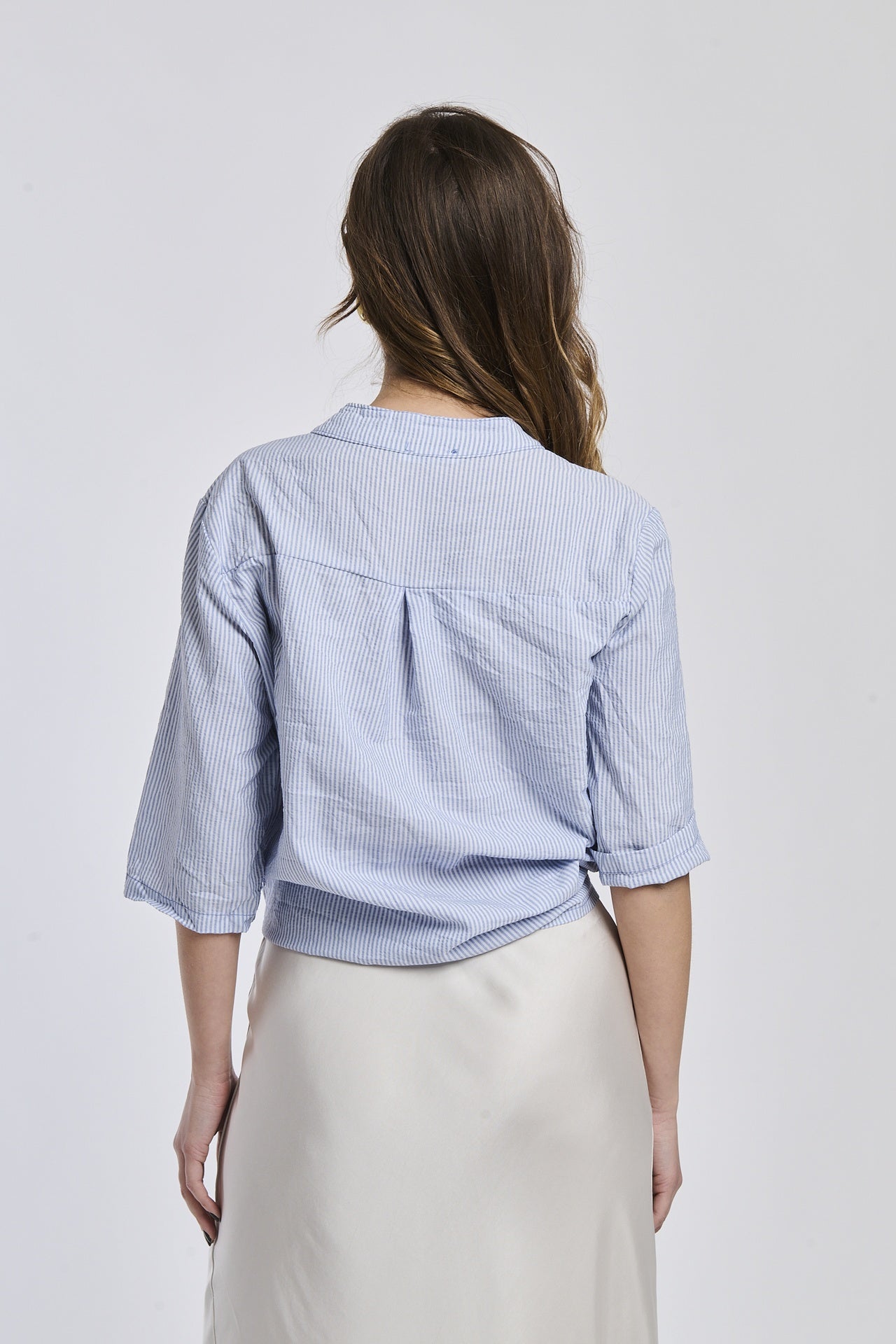 Donna indossa una camicia a righe navy, maniche corte e nodo decorativo, stile preppy e raffinato.