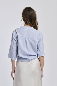 Donna indossa una camicia a righe navy, maniche corte e nodo decorativo, stile preppy e raffinato.