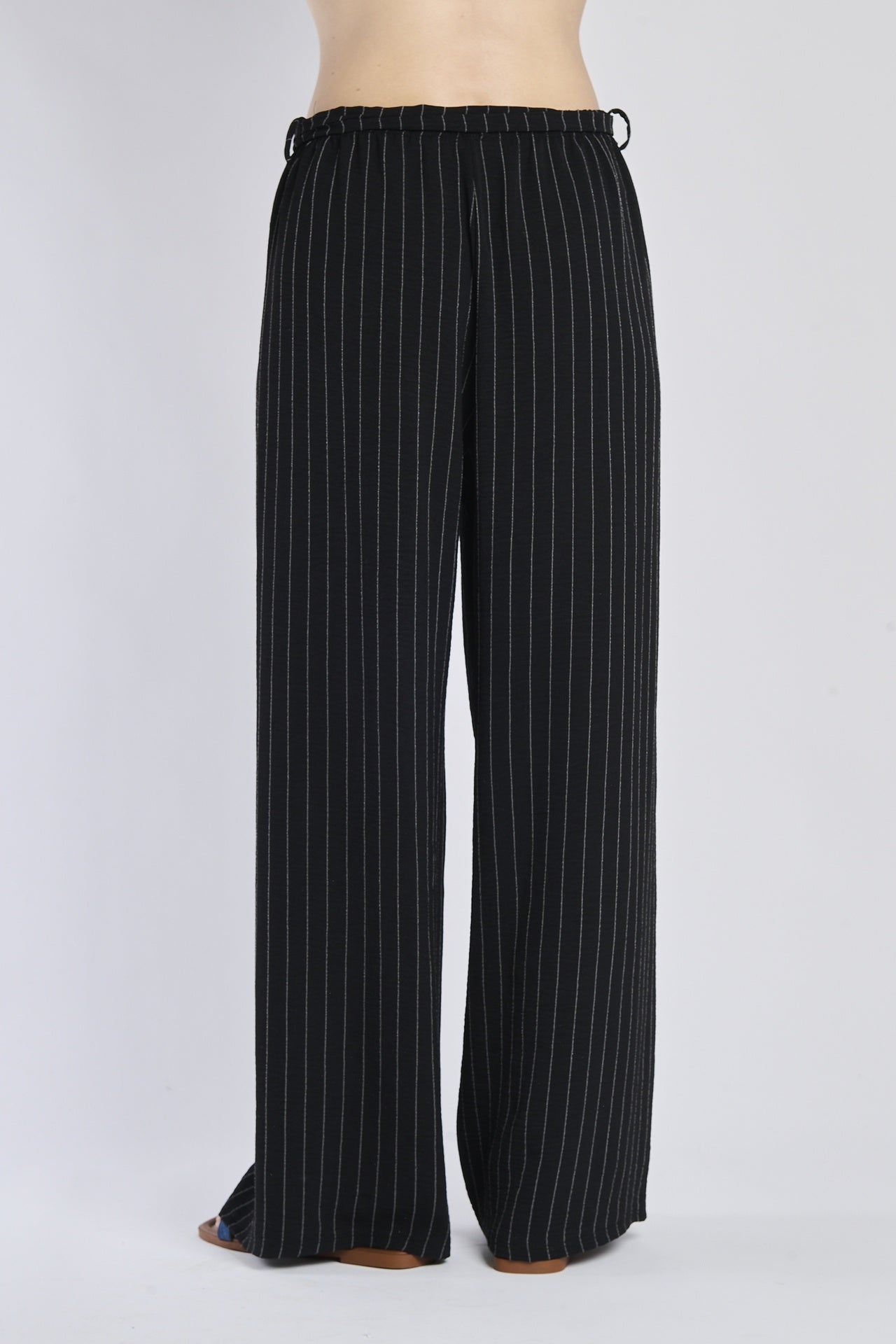 Pantaloni larghi neri con coulisse e nodo in vita, abbinati a sandali.