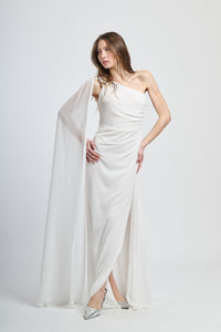 Abito lungo bianco, spalla singola, drappeggio fluido, accessorio decorativo sulla spalla.