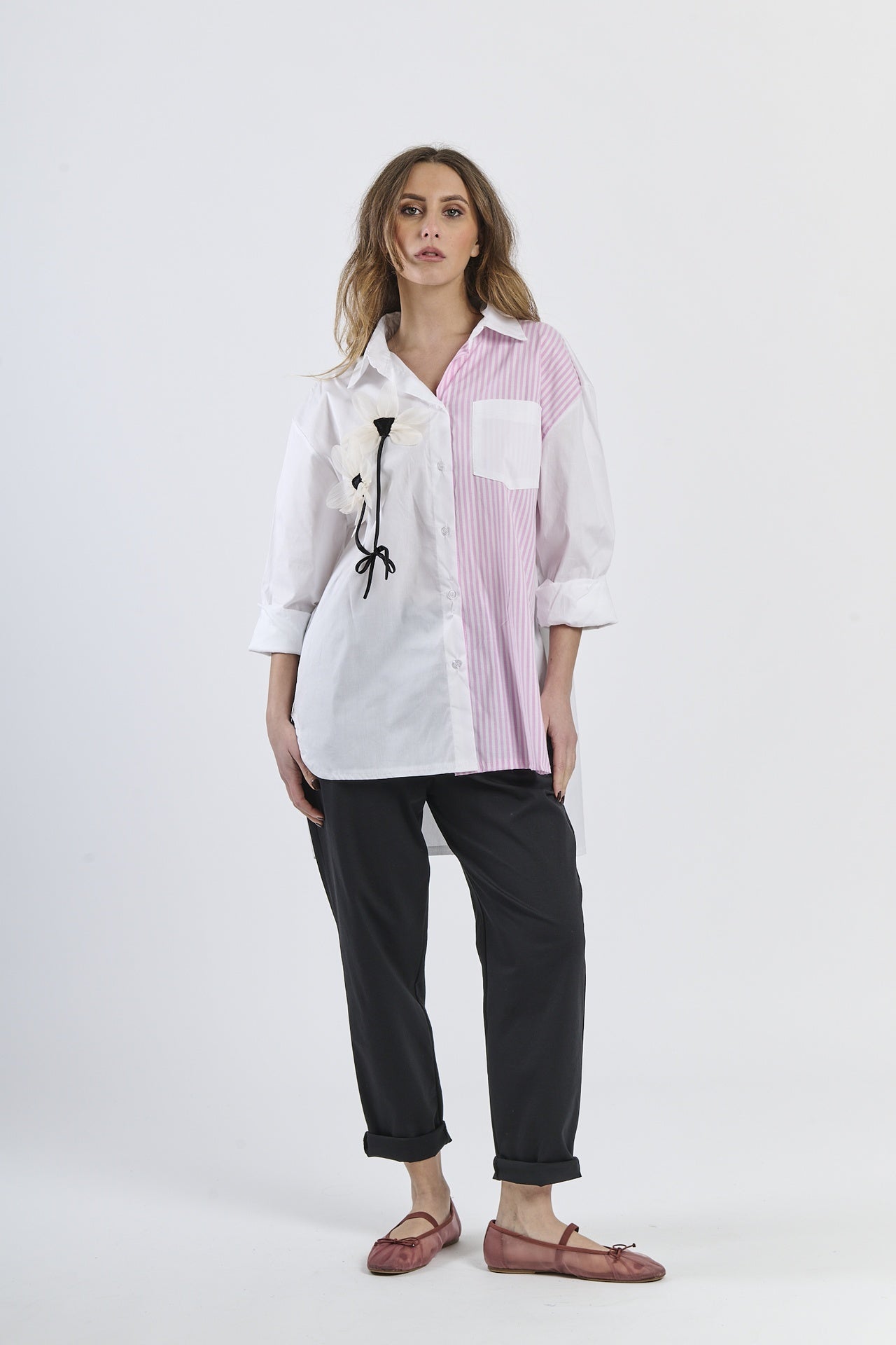Camicia oversize bicolor bianca e rosa a righe, con fiore decorativo e tasca contrastante, abbinata a pantaloni scuri e mocassini rossi