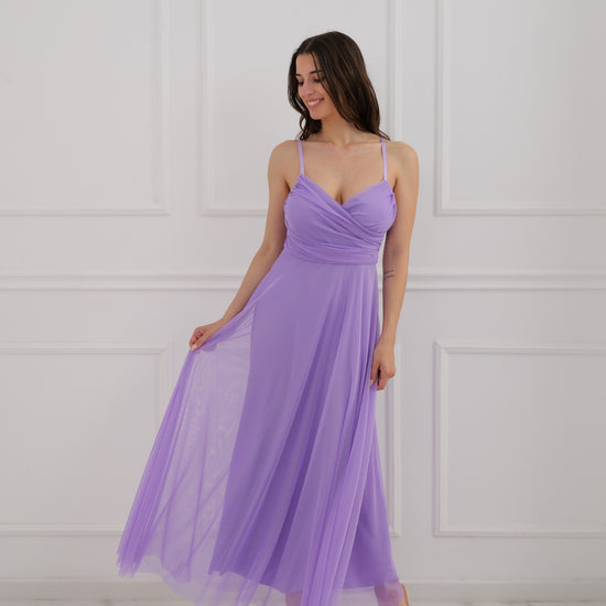 Donna con abito viola a spalline, taglio ampio sulla schiena, posa con una mano sulla vita