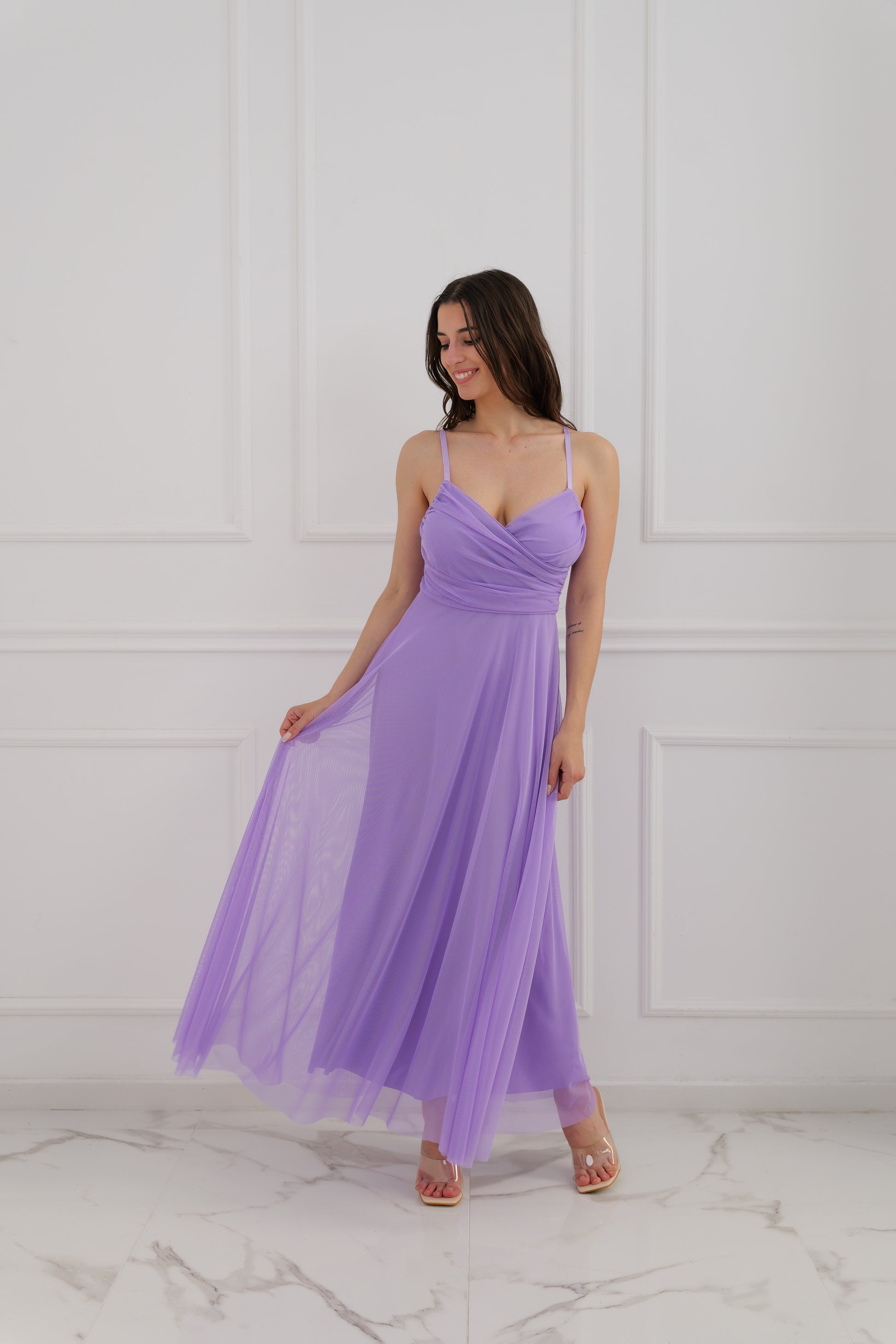 Donna con abito viola a spalline, taglio ampio sulla schiena, posa con una mano sulla vita