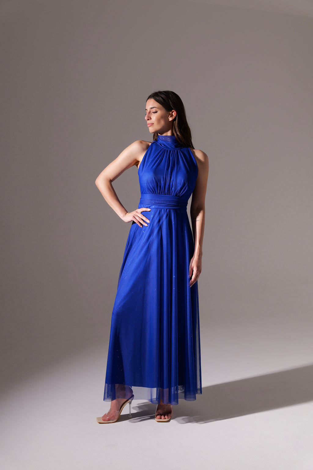 Donna in abito blu scuro fluido, colletto alto, posa con bracci alzati per esibire il vestito