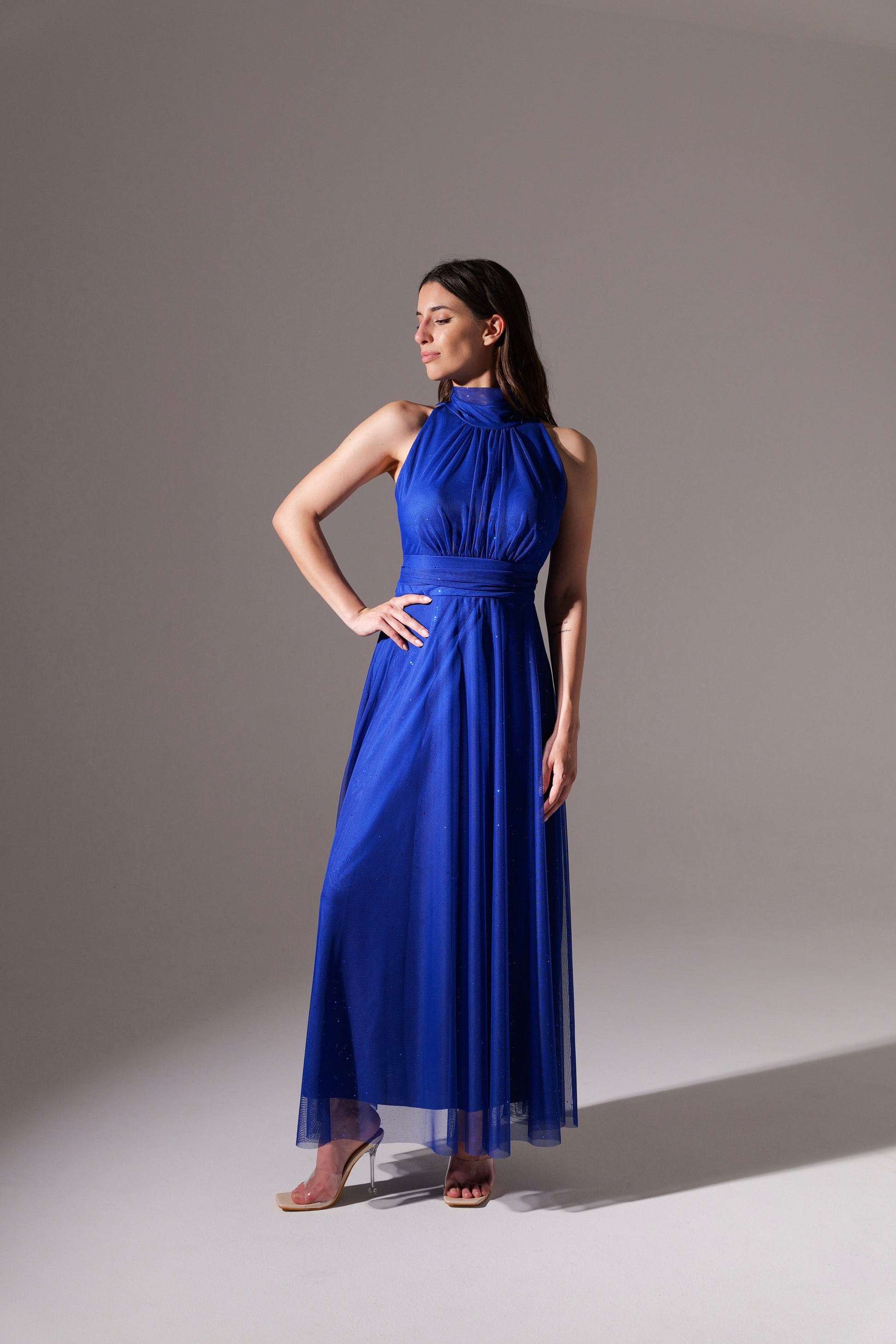 Donna in abito blu scuro fluido, colletto alto, posa con bracci alzati per esibire il vestito